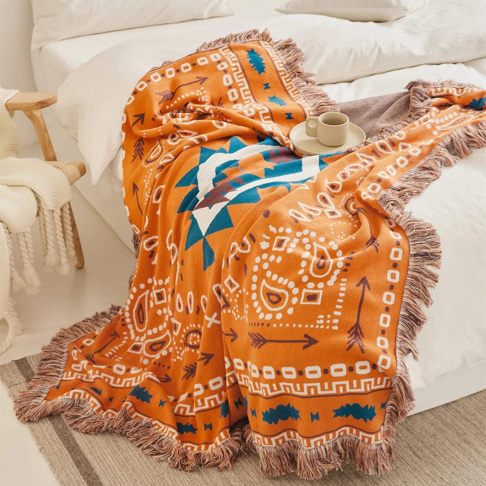 Orange bohemian jacquard cotton throw blanket with fringes, draped on a white bed with a coffee cup.