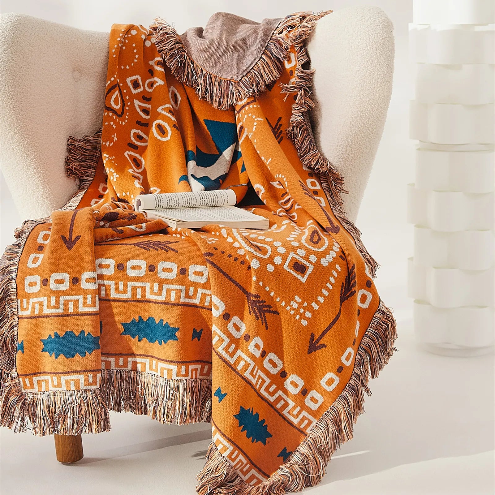 Orange bohemian jacquard cotton throw blanket with fringes and patterns draped over a white wingback armchair.