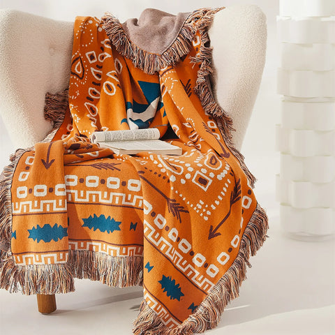 Orange bohemian jacquard cotton throw blanket with fringes and patterns draped over a white wingback armchair.