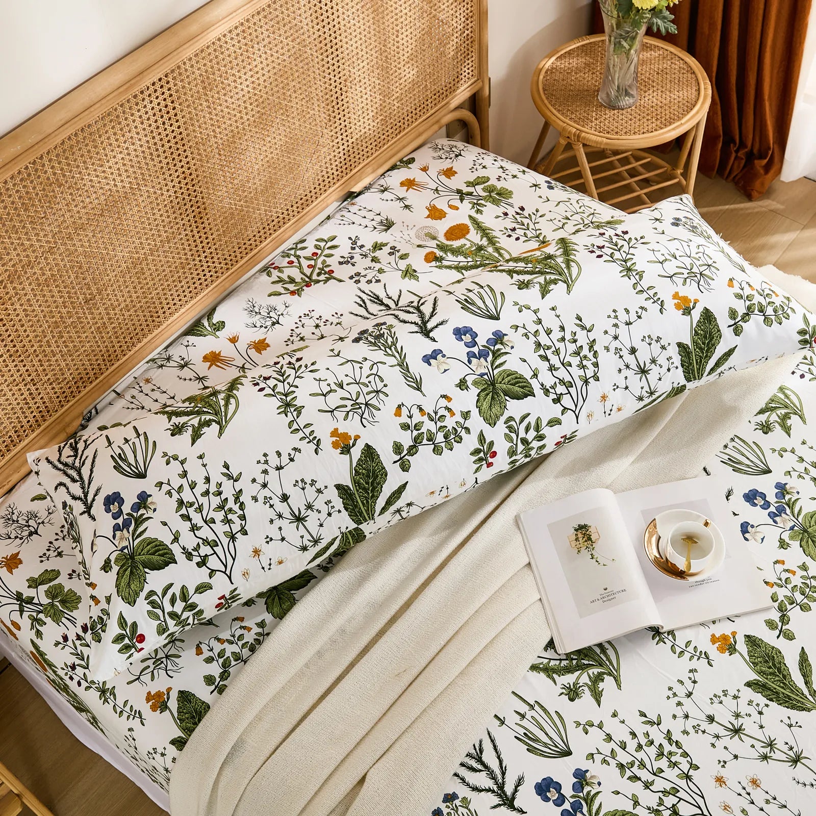 An overhead shot of a long white cotton body pillow with a vibrant botanical print, resting on a bed with a matching sheet and blanket.