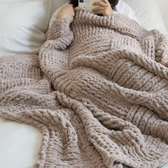 A person is comfortably wrapped in a soft taupe chunky knit blanket, highlighting its warmth and luxurious feel