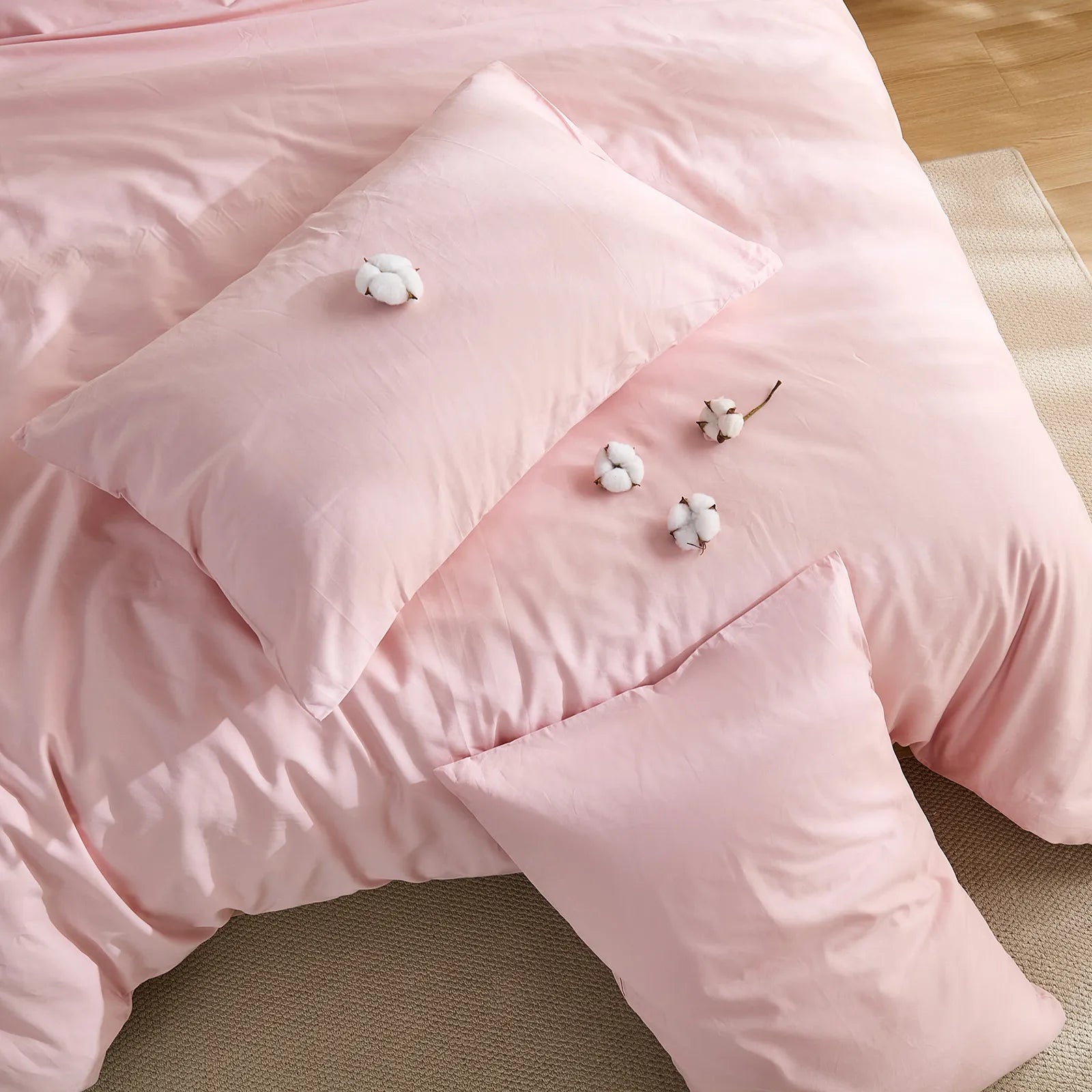 Pink solid duvet layout with cotton buds and two pillows arrangement