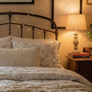 detailed shot of poetic meadow floral bedding under the warm glow of a bedside lamp