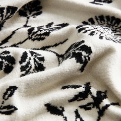 A close-up of the elegant microfiber blanket, highlighting the delicate ruffled edge and black leaf pattern.