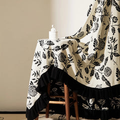An elegant ruffled microfiber blanket with a black leaf pattern, styled as a chic bed throw for a luxurious feel.