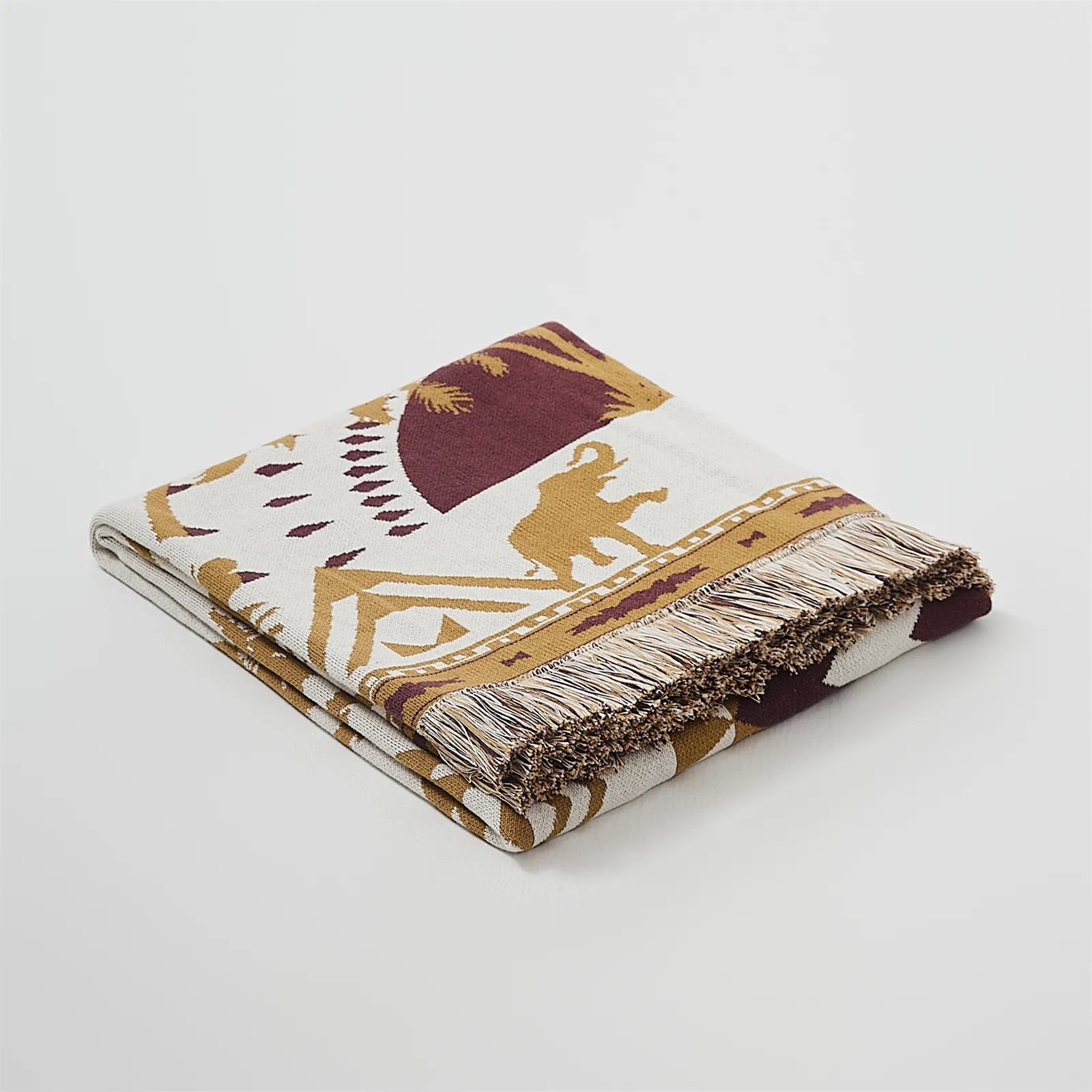 A studio shot of a perfectly folded sand yellow bohemian tassel blanket, highlighting its material and beautiful color.