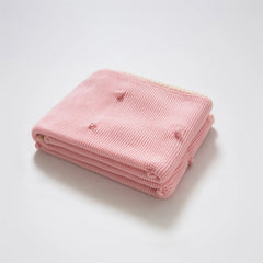 Neatly folded soft pink cotton knit throw blanket with cream fringe trim and bobble texture