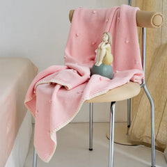 Soft pink cotton knit throw draped over a modern chair with a figurine decoration
