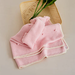Soft pink cotton bobble throw flatlay with bamboo basket and green plant on beige background