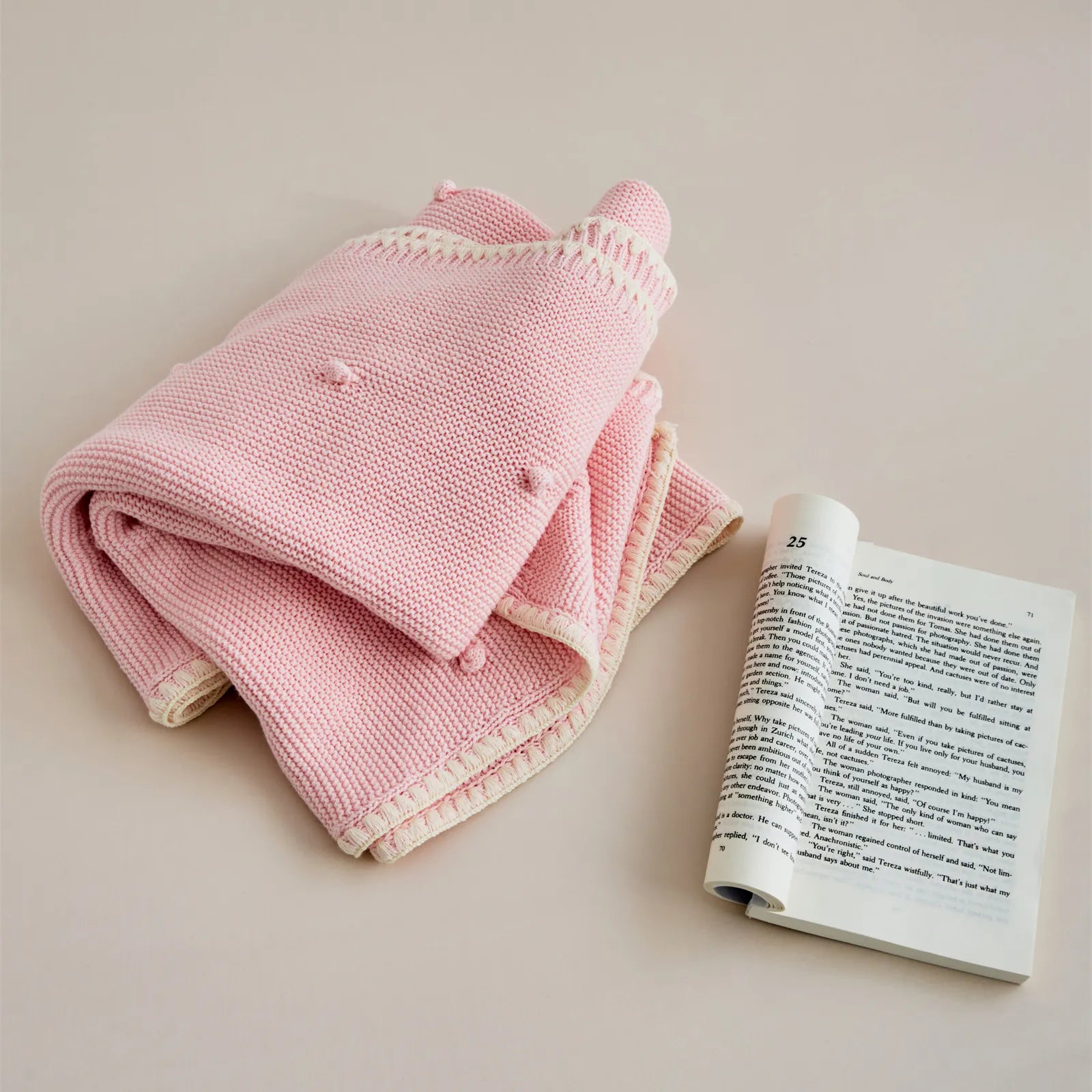 Soft pink cotton knit throw folded beside an open book in a minimal, warm setting