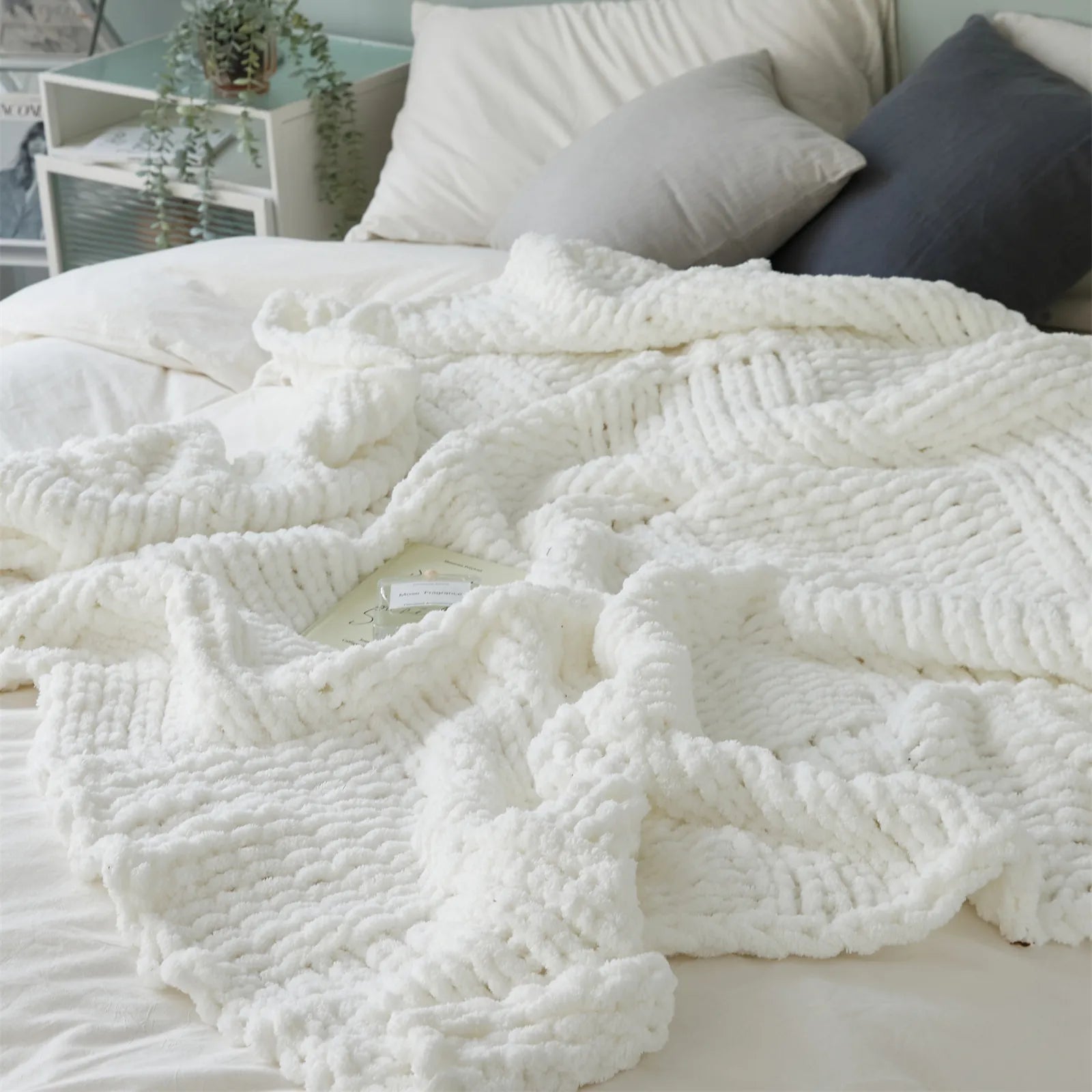 A close-up view of the white chunky knit blanket styled on a bed, showcasing its fluffy, woven texture and inviting feel