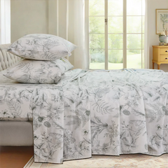 Stacked cotton greenery print pillows on sheet set with large window and daylight