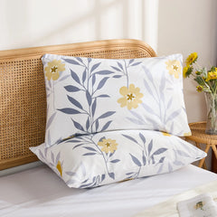 Two white cotton pillowcases featuring a contemporary yellow floral and grey leaf pattern, stacked neatly on a bed.