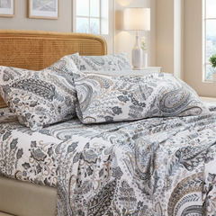 Stacked cotton neutral paisley print pillows on fitted sheet set on white bed