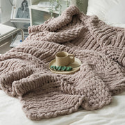 A plush taupe chunky knit blanket is spread out on a white bed, with a mug on a tray, creating a warm, cozy scene.