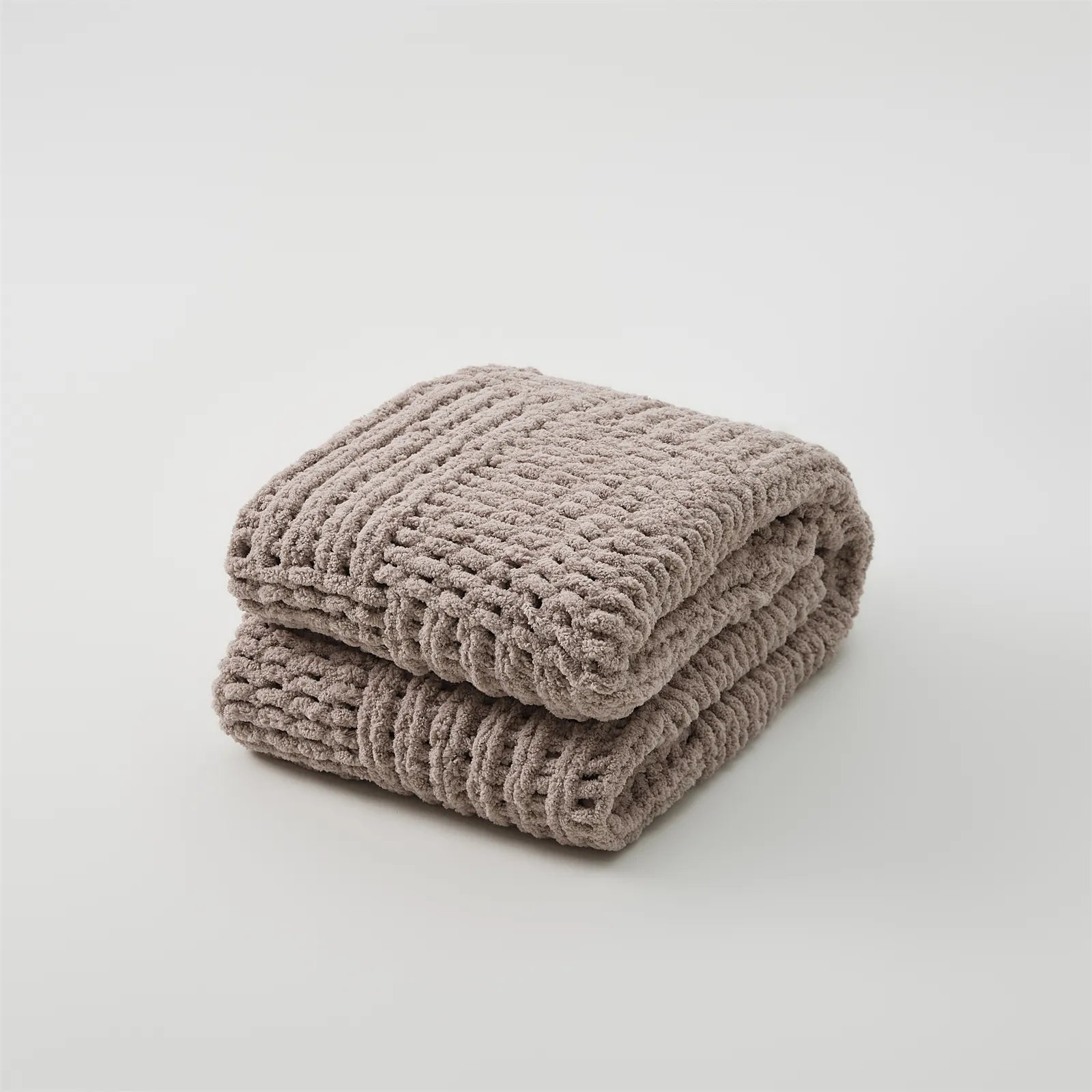 A studio shot of a perfectly folded taupe chunky knit blanket, highlighting its rich color and thick, woven texture