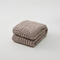 A studio shot of a perfectly folded taupe chunky knit blanket, highlighting its rich color and thick, woven texture