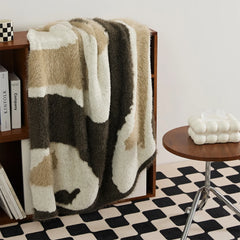 Soft abstract knit blanket in warm taupe and mocha folded and displayed on dark wooden shelf