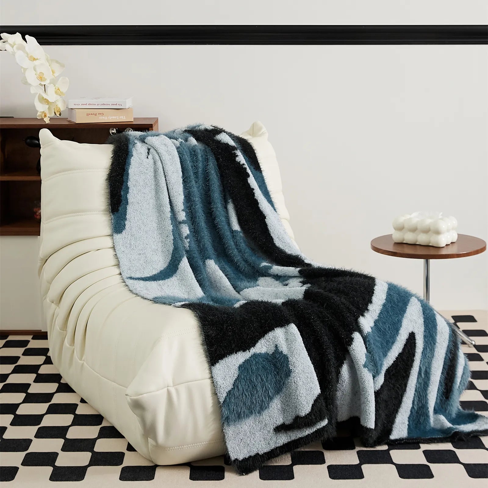 Stylish teal and denim blue abstract fuzzy throw draped on white leather Togo sofa