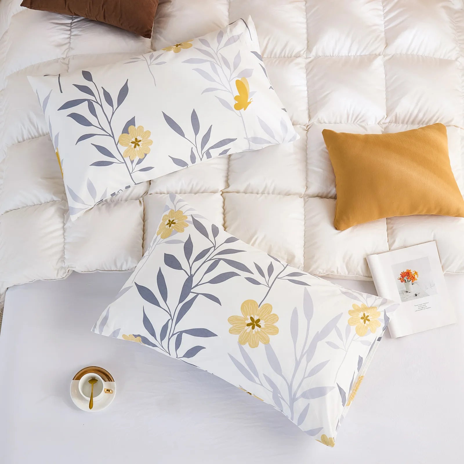 An overhead shot of a bedding set with two white cotton pillowcases and a matching sheet featuring a modern floral print, on a fluffy white comforter.