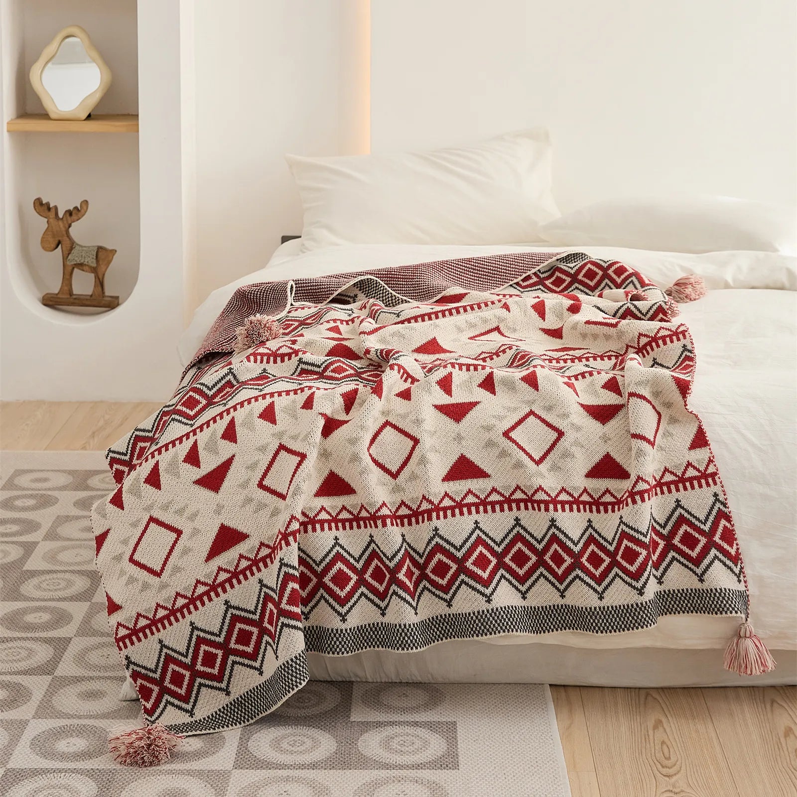 Vintage boho geometric knit throw blanket with tassels spread over a white bed