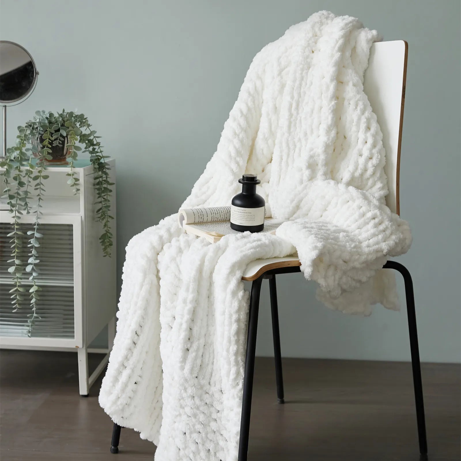 A thick, white chunky knit blanket draped elegantly over a modern chair, perfect as a stylish and cozy home decor accent.