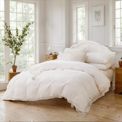 A bright bed with a layered white cotton ruffle duvet cover and pillows, flanked by nightstands with lamps.