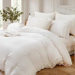 A bed made with a white cotton ruffle duvet cover, multiple pillows, and a casually draped knitted blanket.