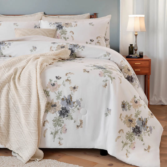 Angled view of a bed with a white floral comforter set, beige knit blanket, and a wood nightstand