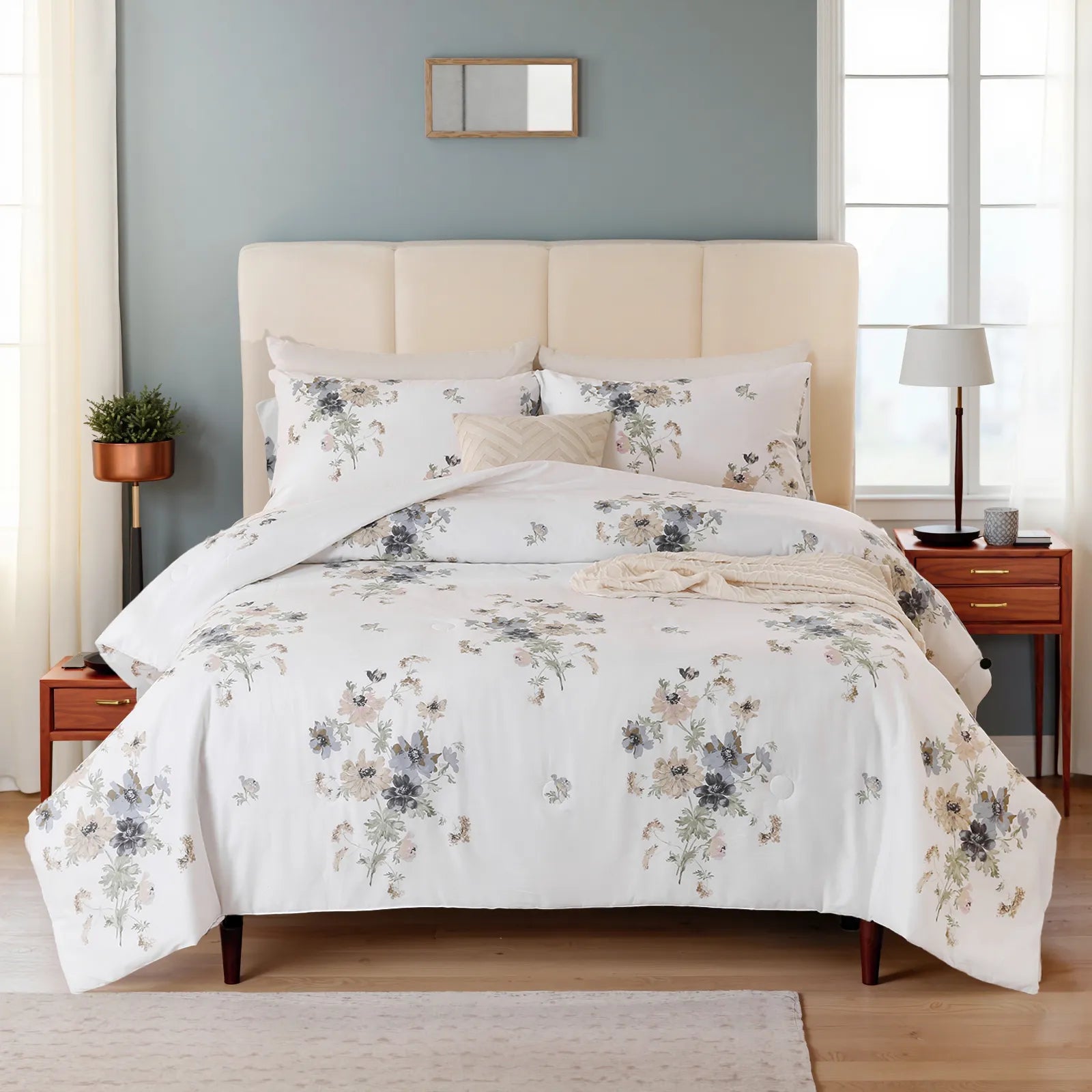 Wide shot of a bed with a white floral comforter set, light blue walls, and a wood nightstand